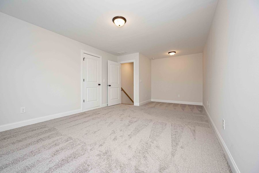 Empty room with light gray carpet and white walls, two doors, and stairs.