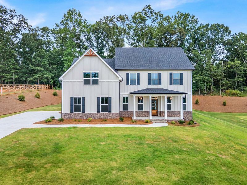 Two-story house with light gray siding, black shutters, and a green lawn against a backdrop of trees.
