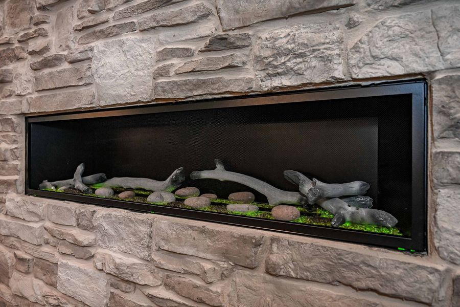 Modern linear fireplace built into a stone wall, featuring logs, rocks, and green moss.