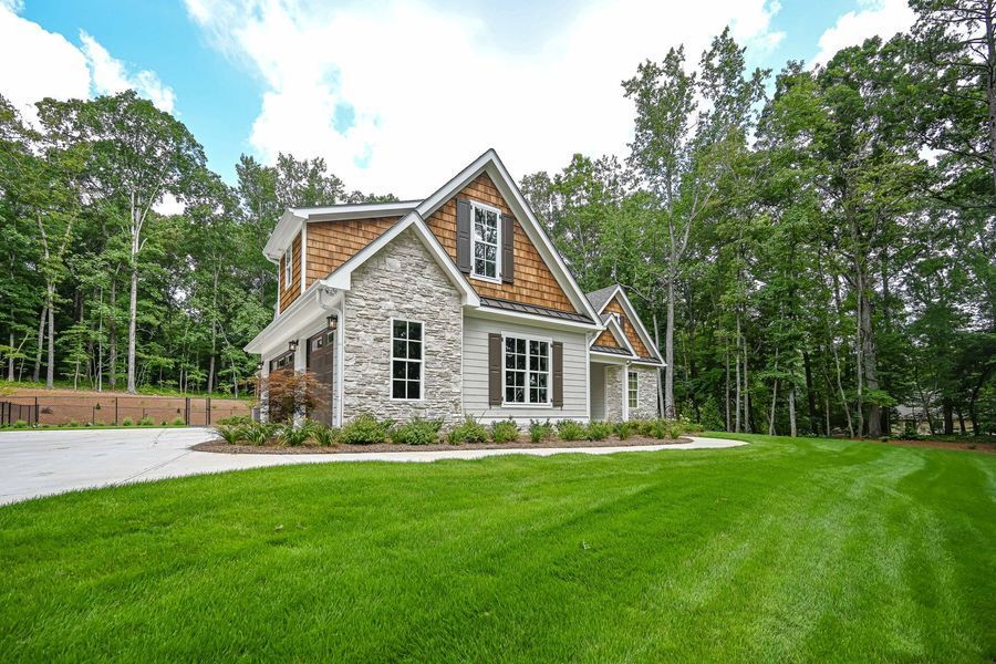 Stone and wood home with green lawn, trees in background, under a blue sky.