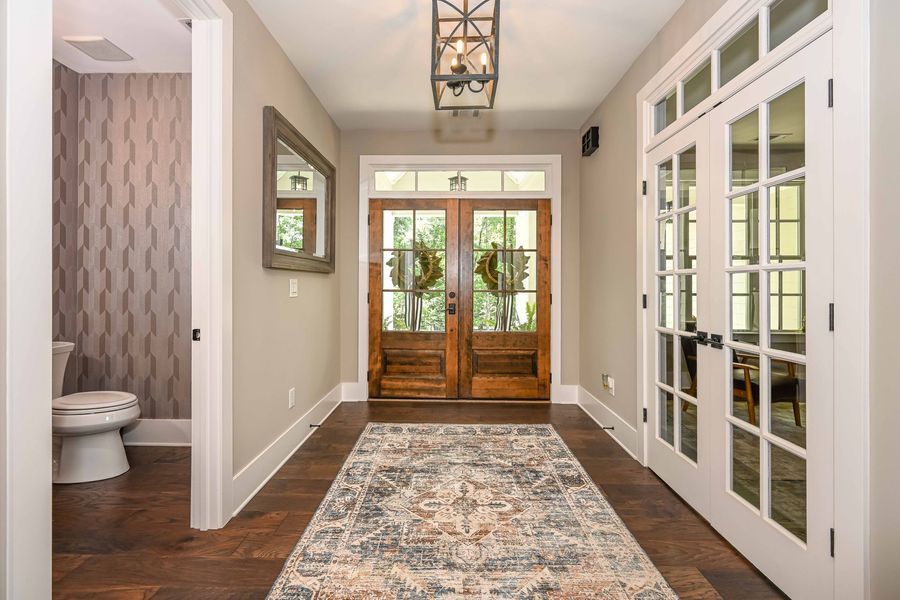 Hallway with dark wood floors, area rug, double wooden doors, and a powder room.
