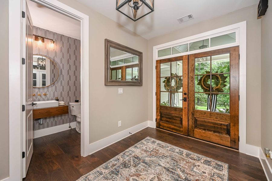 Entryway with wood double doors, rug, mirror, and powder room door.