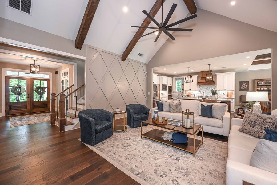 Living room with dark wood floor, blue chairs, white sofa, and kitchen in the background.