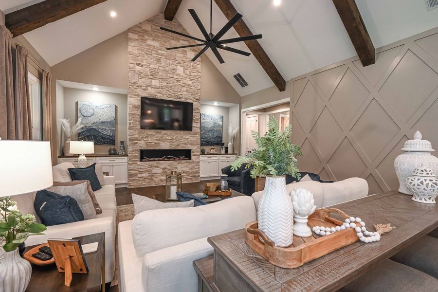 Living room with stone fireplace, white sofas, wooden beams, and a large black ceiling fan.