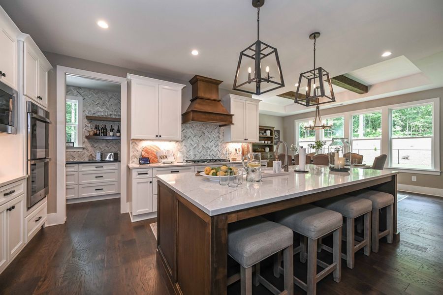 Spacious kitchen with white cabinets, dark island, marble countertops, and pendant lights