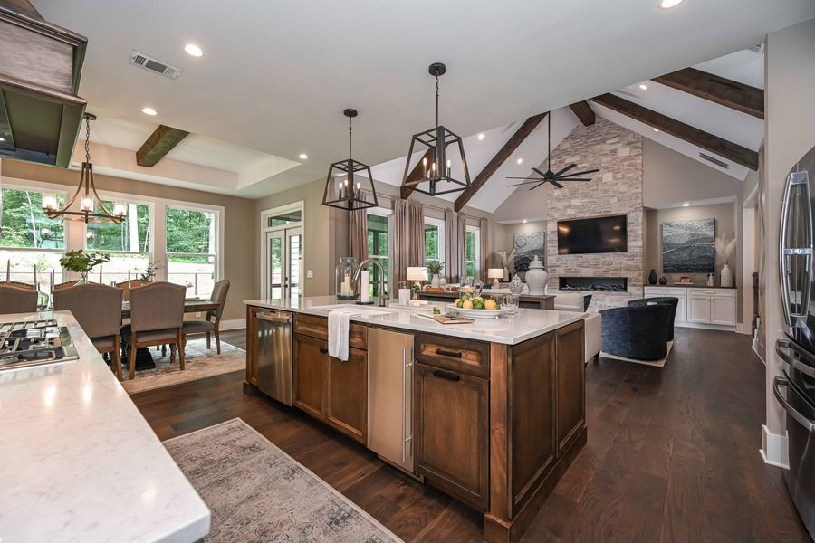 Open-concept kitchen with island, dining area, and living room; wood floors, neutral colors, and stone fireplace.