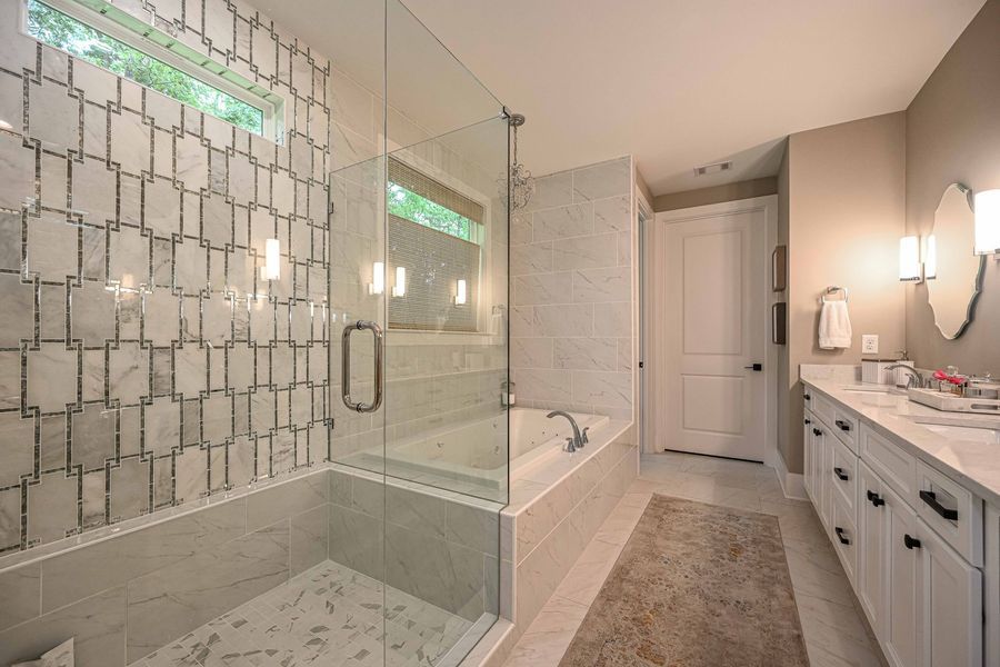 Modern bathroom with glass shower, patterned tile wall, tub, vanity with double sinks.