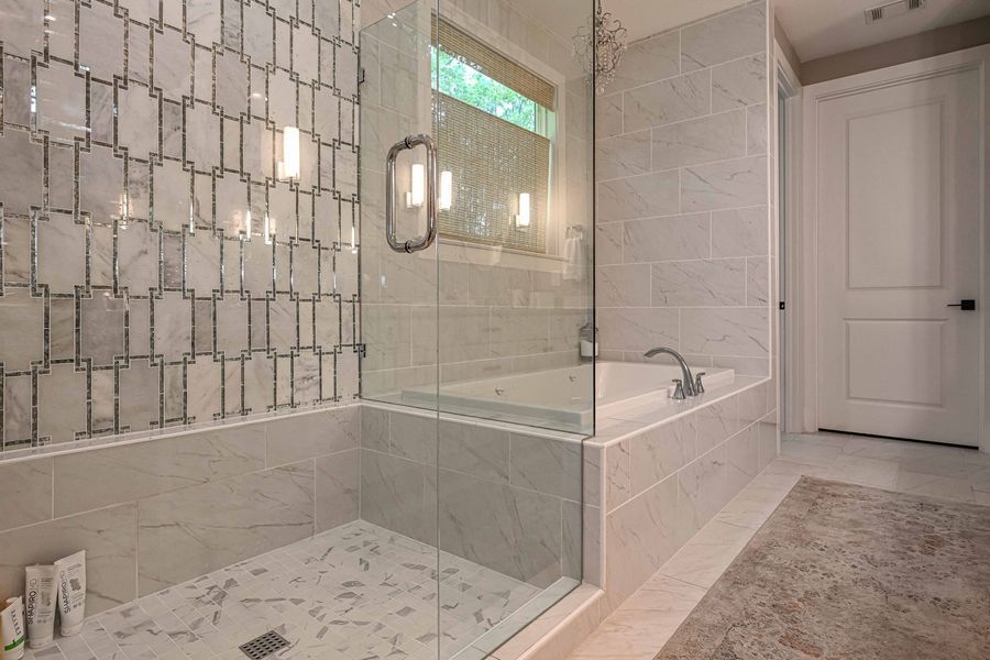 Modern bathroom with glass shower, marble tile, and a jacuzzi tub.