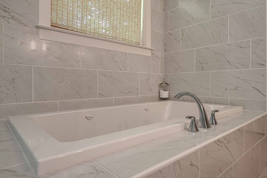 A white bathtub with a chrome faucet, against marble-patterned tile walls.