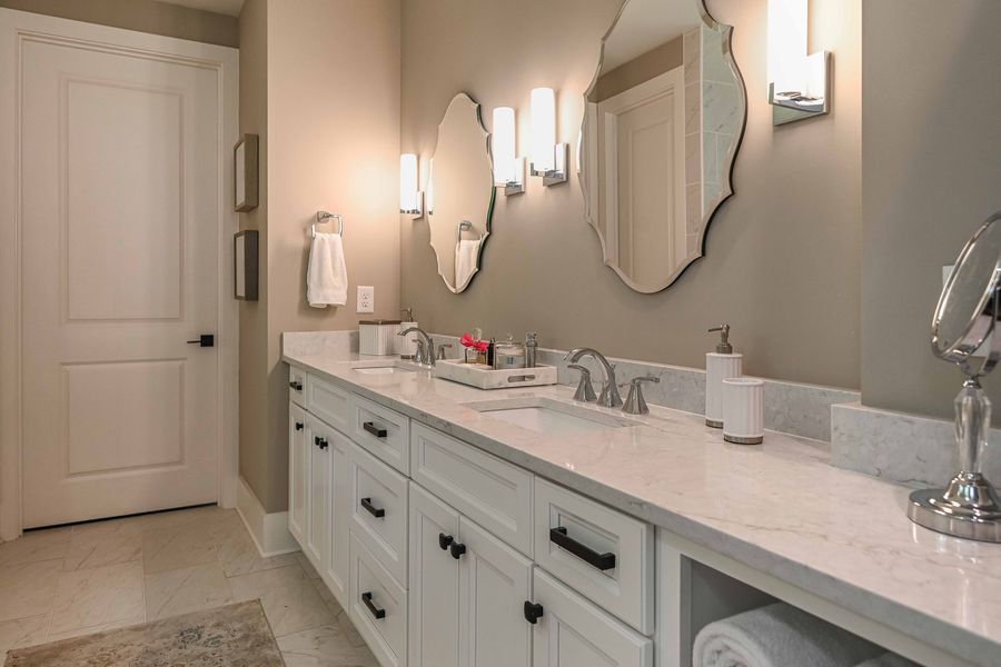 Bathroom with white vanity, two sinks, wavy mirrors, sconces, and white door.