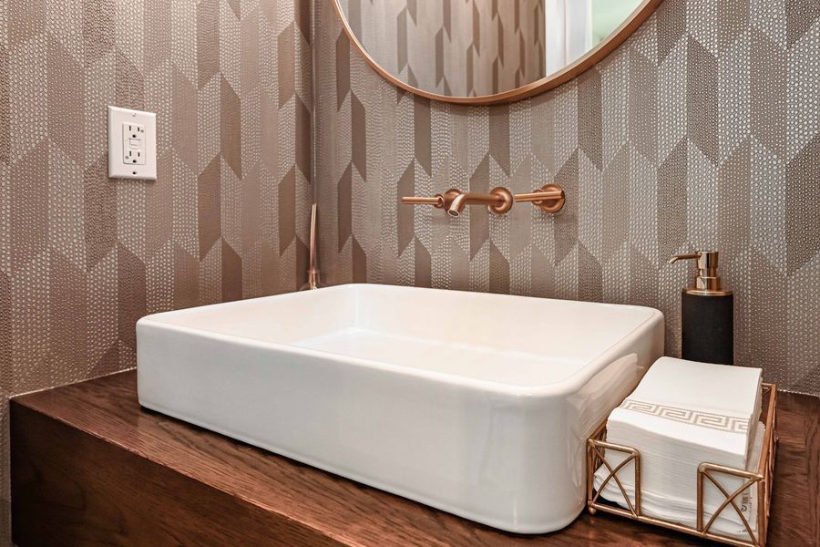 Modern powder room: white rectangular sink on wood counter, copper fixtures, patterned metallic wallpaper.