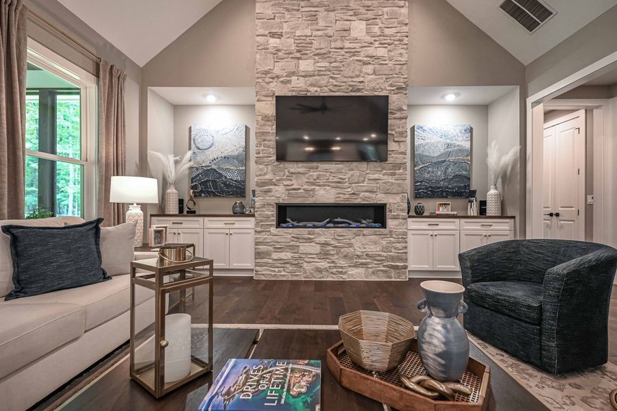 Living room with stone fireplace, TV, built-ins, sofa, and armchair.