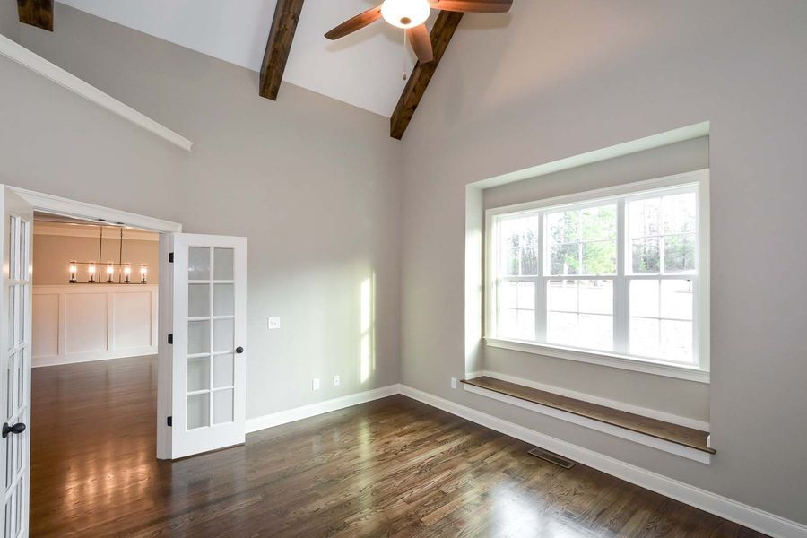 Empty room with dark wood floors, gray walls, and a window seat. French doors lead to another room.
