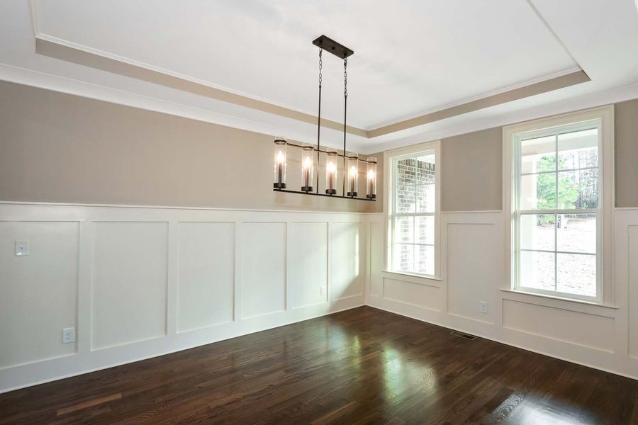 Dining room with dark wood floors, beige walls, white trim, and chandelier.