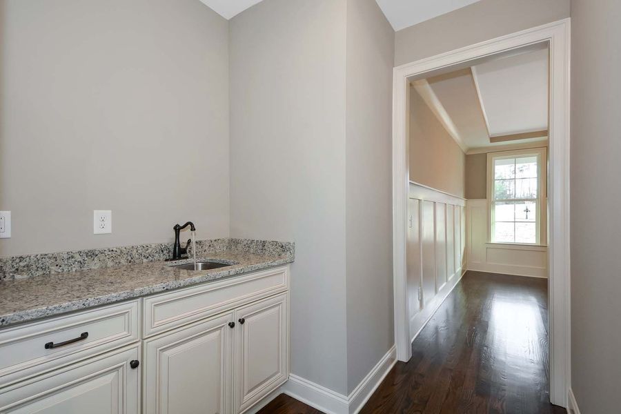 Small gray room with a sink and cabinets, doorway leads to hallway with window.