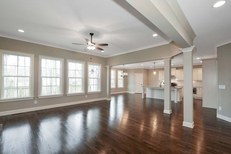 Spacious living area with dark wood floors, tall windows, and a kitchen in the background.