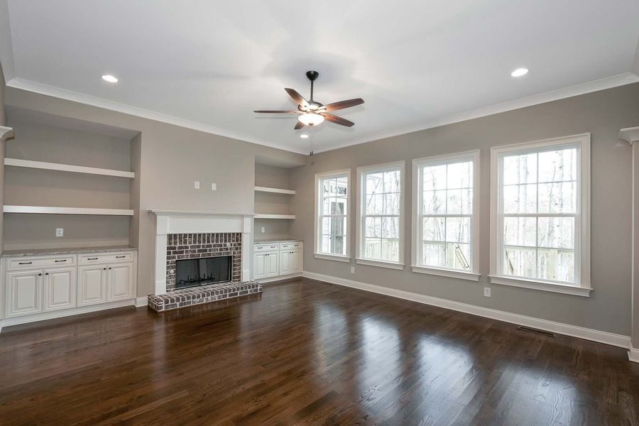 Living room with fireplace, built-in shelves, hardwood floor, and large windows; neutral tones.