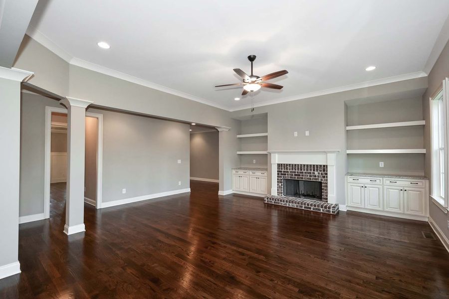 Spacious living room with dark hardwood floors, gray walls, fireplace, built-in shelves, and ceiling fan.