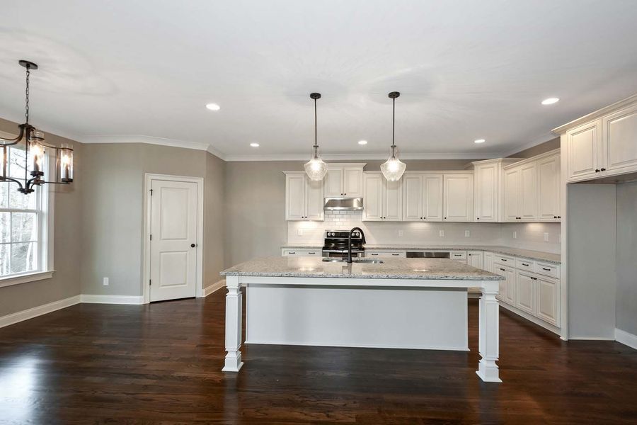 Spacious kitchen with white cabinetry, large island, dark wood floors, and pendant lights.