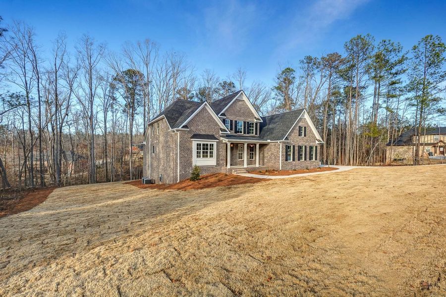 House with brick facade on a grassy lot with trees in the background on a sunny day.
