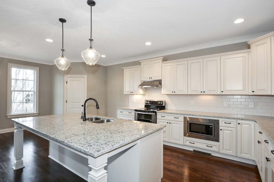 Bright kitchen with white cabinets, granite countertops, dark wood floor, and island.