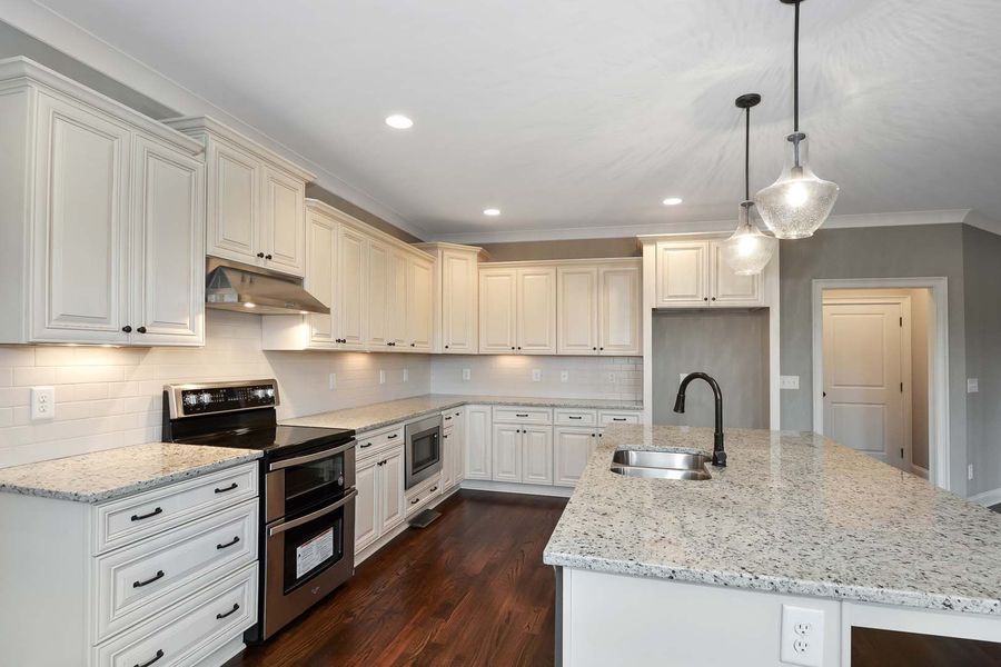 Creamy white kitchen with granite countertops and stainless steel appliances. Dark wood floors.