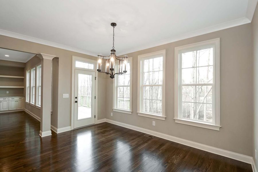 Dining room with three windows, a door, and a chandelier, with dark wood floors and beige walls.