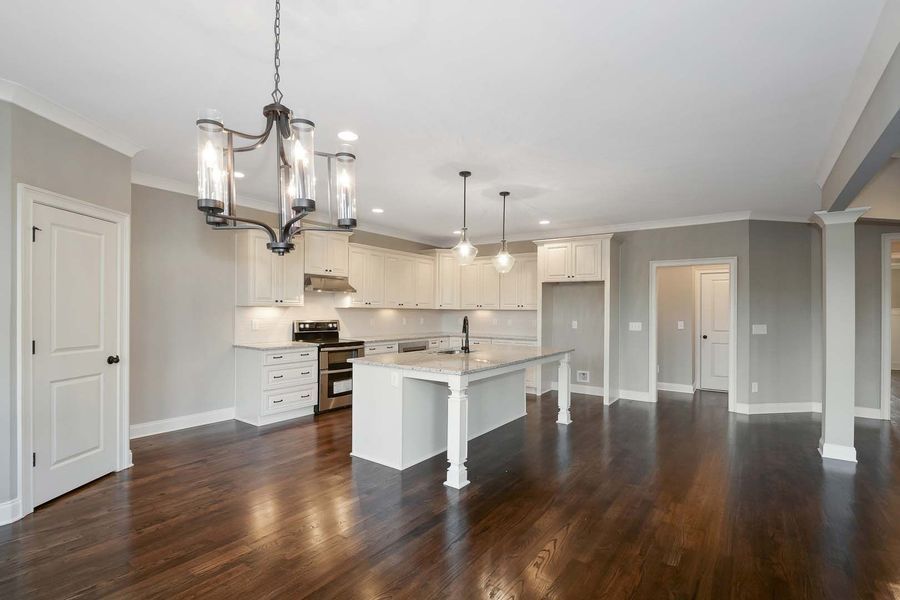 Spacious, light-filled kitchen and living area with hardwood floors, white cabinets, and a chandelier.