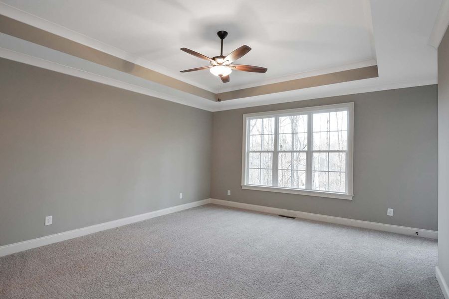 Empty bedroom with gray walls, carpet, window, and ceiling fan.