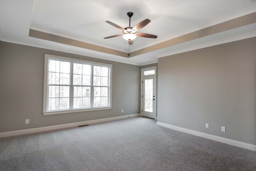Empty bedroom with grey walls, carpet, and ceiling fan. Window and door on opposite walls.