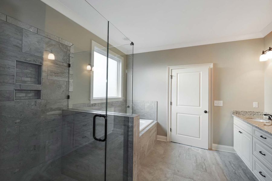 Modern bathroom with a glass shower, gray tile, white cabinets, and a closed white door.