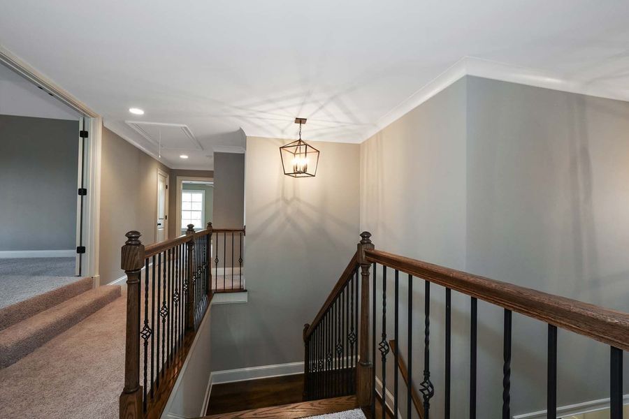 Hallway with stairs, dark wood railing, gray walls, and a hanging light fixture.