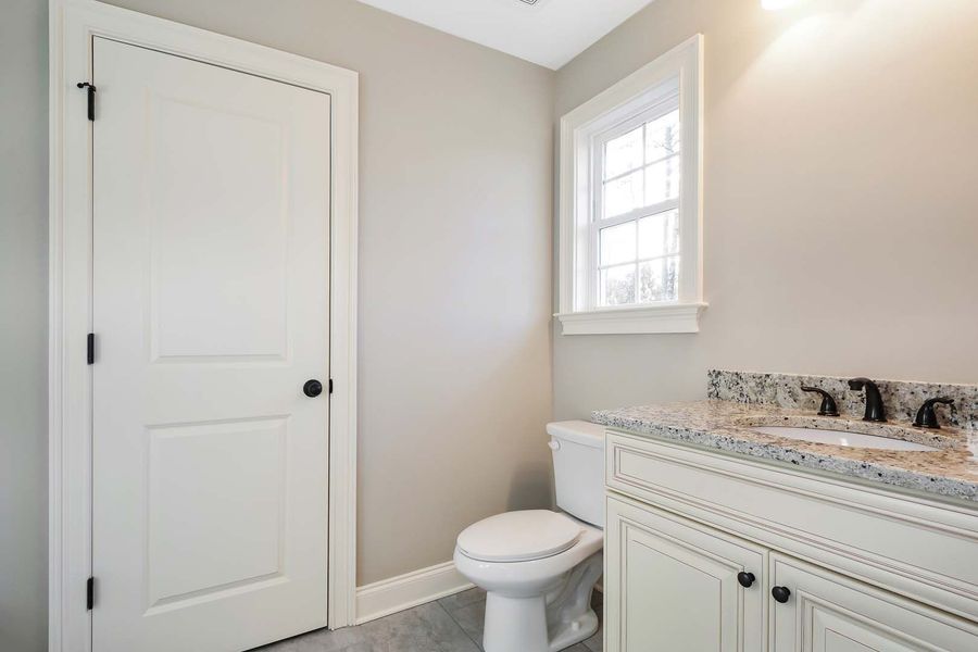 Bathroom with white door, toilet, vanity with granite countertop, and window.