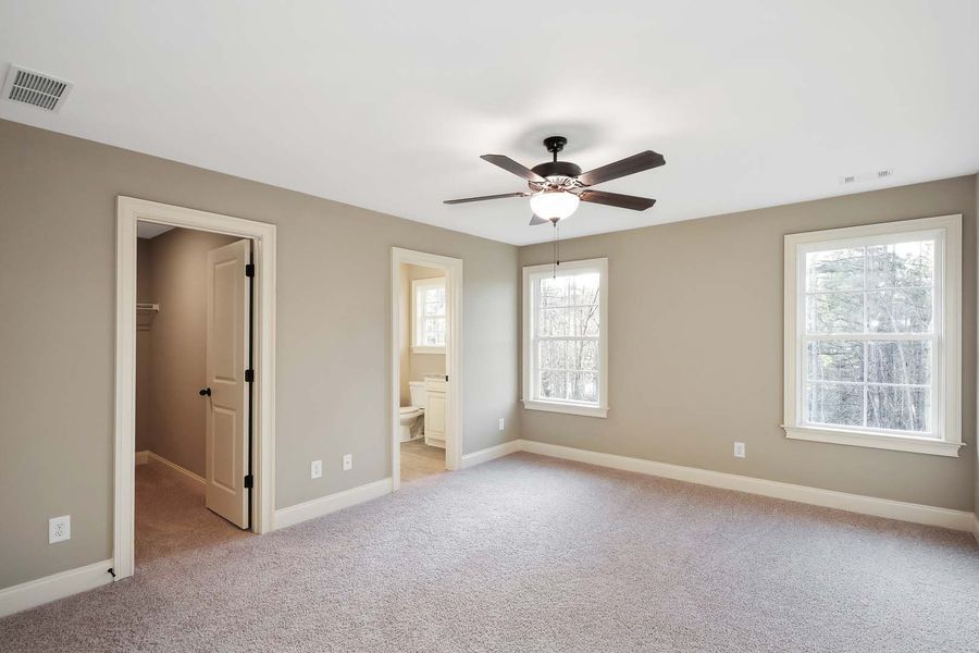 Empty bedroom with neutral-toned walls, carpet, ceiling fan, and doorways to a bathroom and hallway.