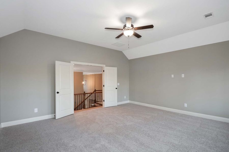 Empty room with gray carpet, walls, and ceiling fan; open doors lead to a staircase.