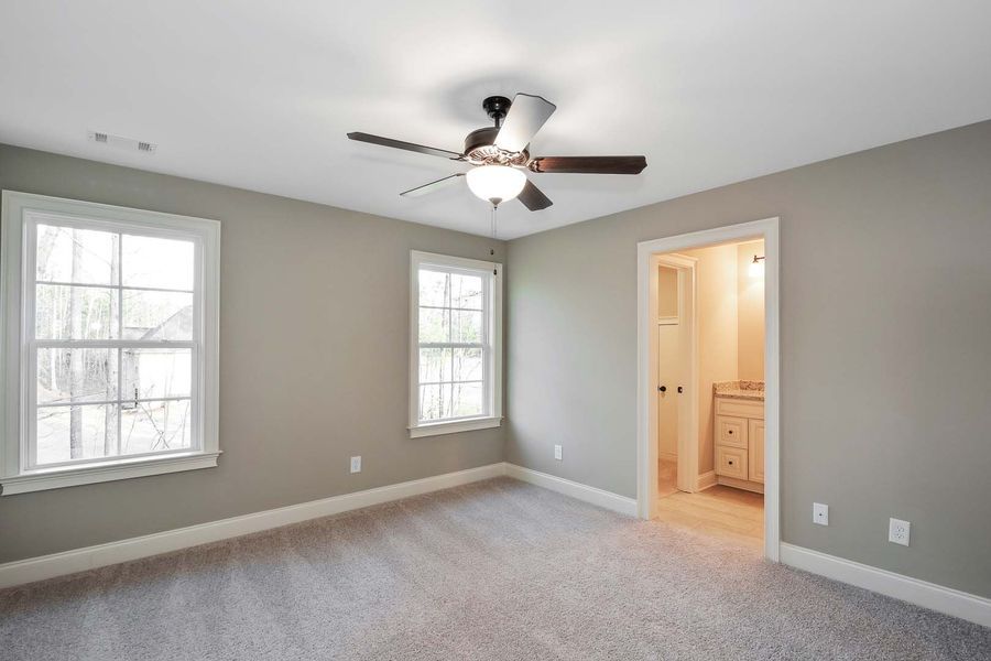Bedroom with gray walls, carpet, two windows, ceiling fan, and doorway to bathroom.