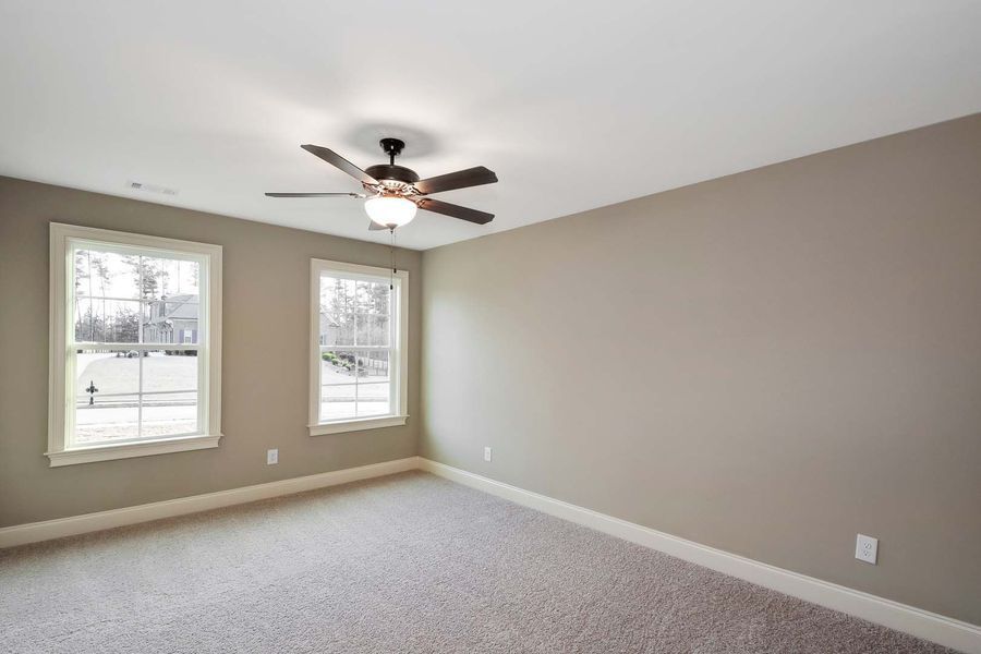 Empty bedroom with beige walls, two windows, ceiling fan, and carpet.
