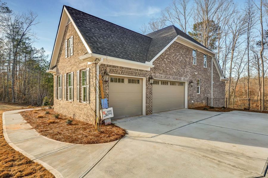 Brick house with two-car garage, gray roof, and concrete driveway.