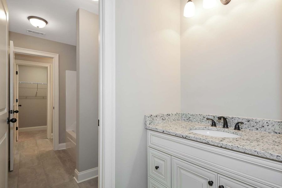 Bathroom with white vanity, granite countertop, and hallway entrance.