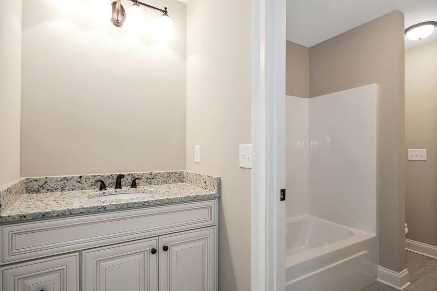 Bathroom with white vanity, granite countertop, and bathtub. Light fixtures on the wall.