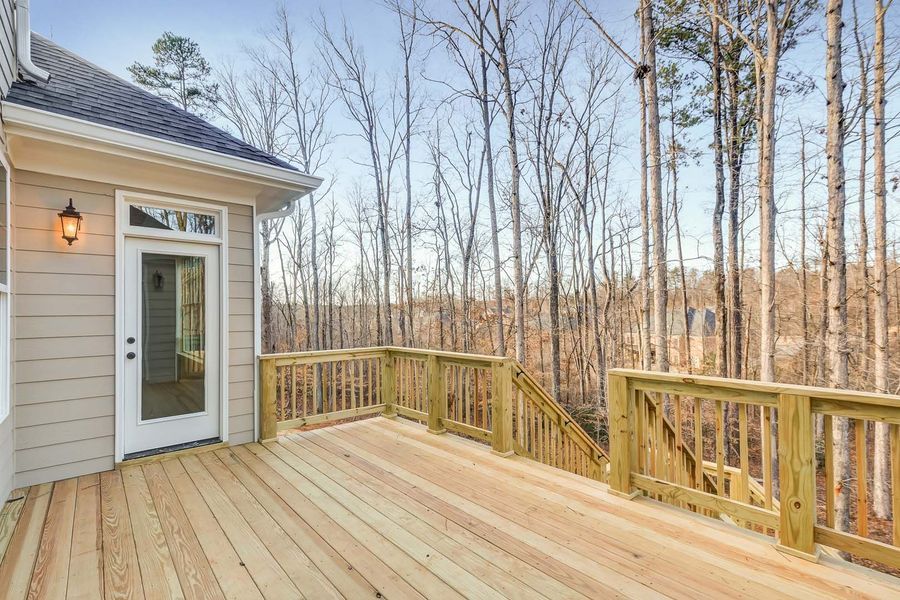 Wooden deck overlooking a forest, with a door to a light-colored house.