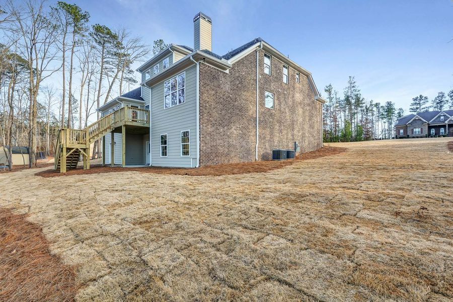 Back of a two-story brick home with a wooden deck, surrounded by a grassy yard, under a blue sky.
