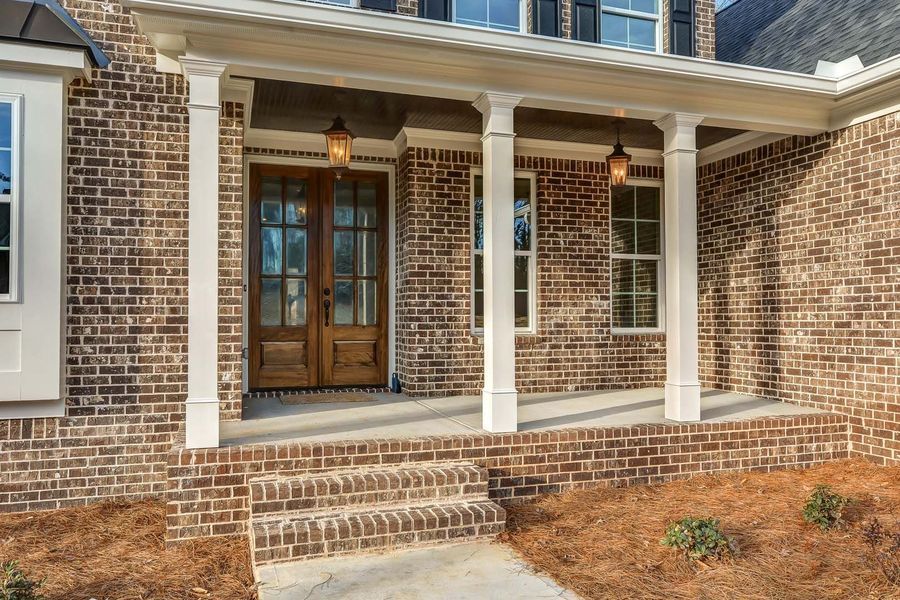 Brick house with a porch, wood doors, and white columns.