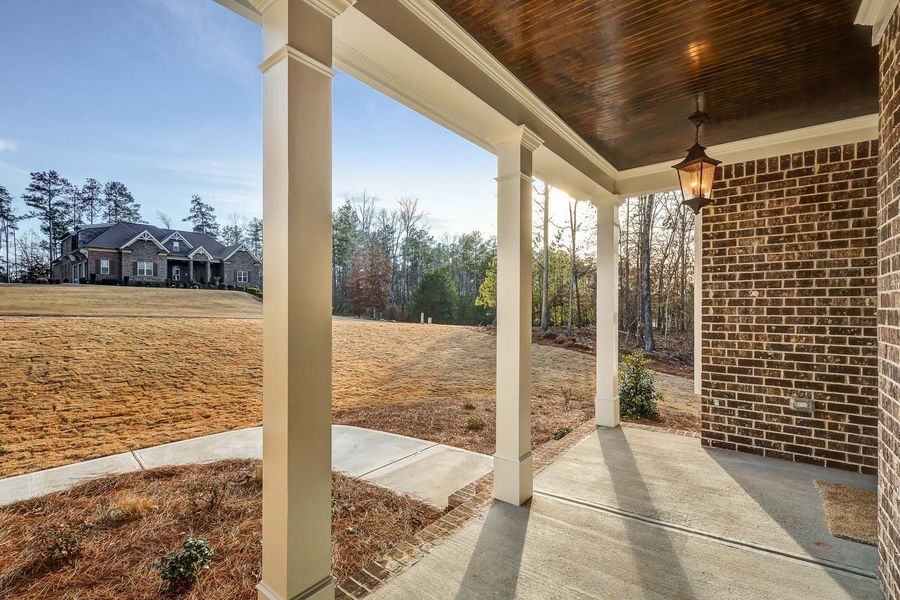 Covered porch with brick wall, white columns, and view of house and yard.