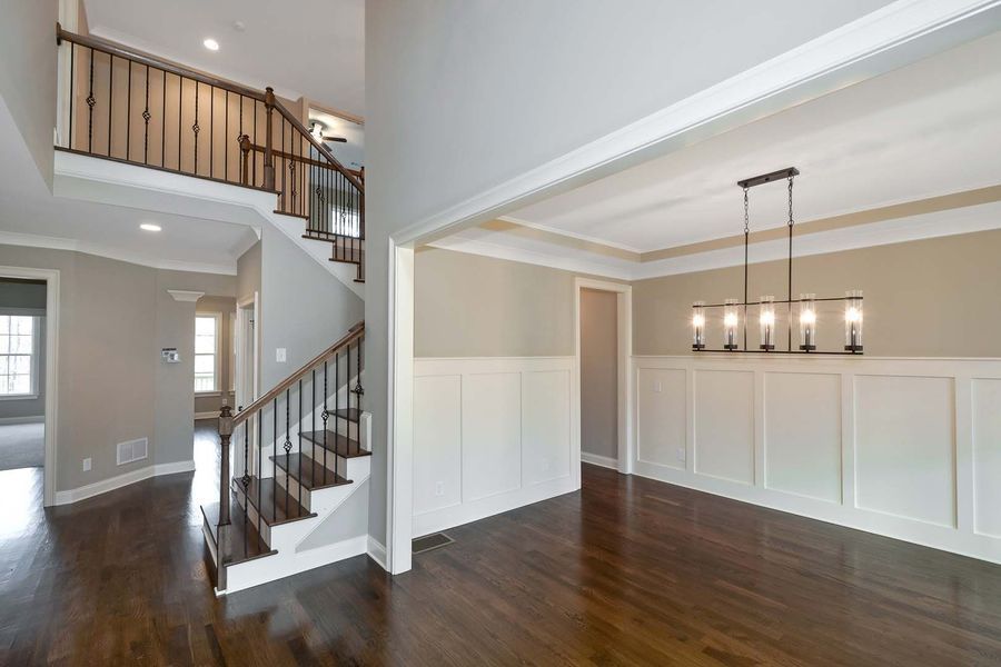 Two-story home interior with staircase, dining room with chandelier, hardwood floors, and neutral-colored walls.