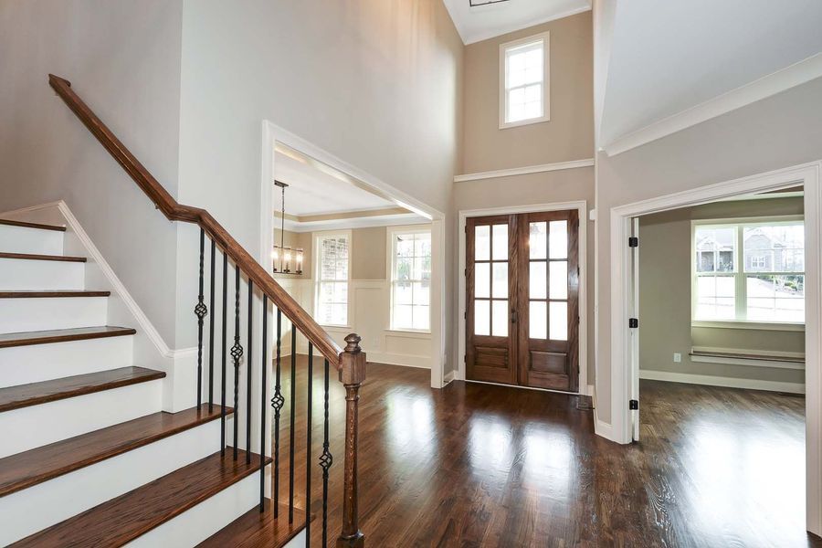 Entryway with staircase, dark wood floor, double doors, and neutral walls.