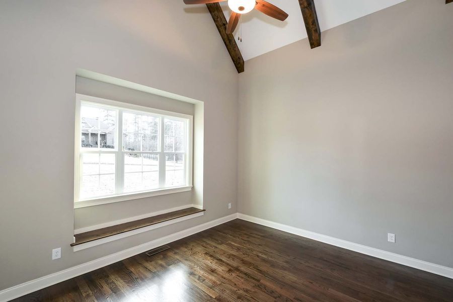 Empty room with wood floor, large window, and high ceiling with exposed beams.