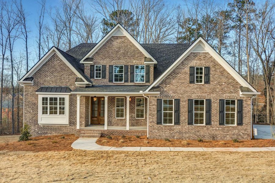 Brick house with dark shutters, porch, and trees.