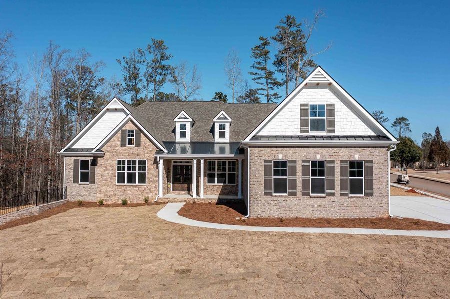 A brick home with a covered front porch, brown shutters, and a gray roof on a sunny day.