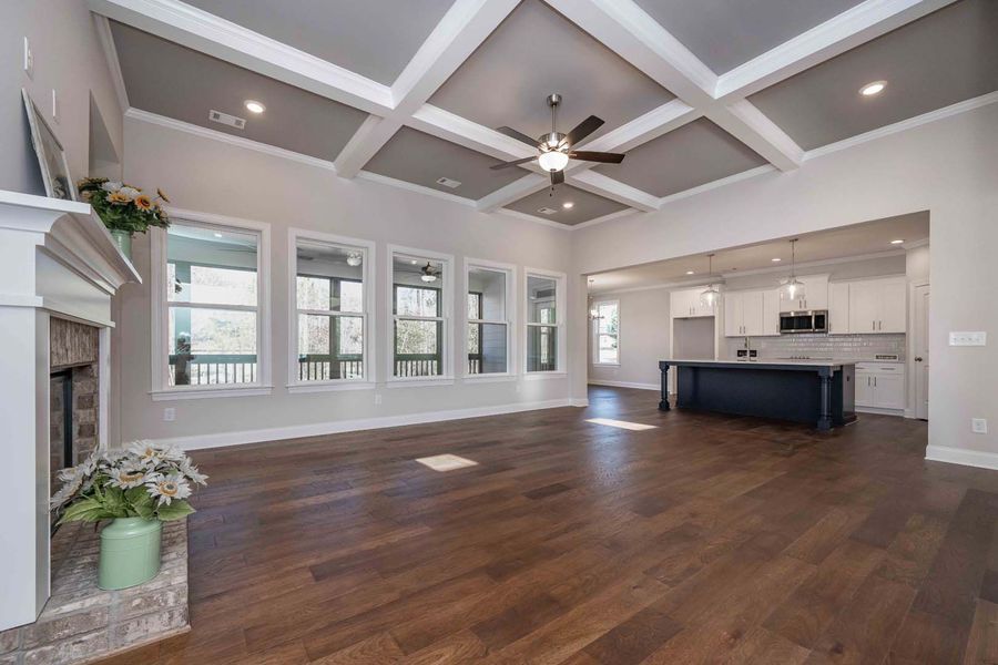 Spacious living room with hardwood floors, a coffered ceiling, fireplace, and kitchen in the background.